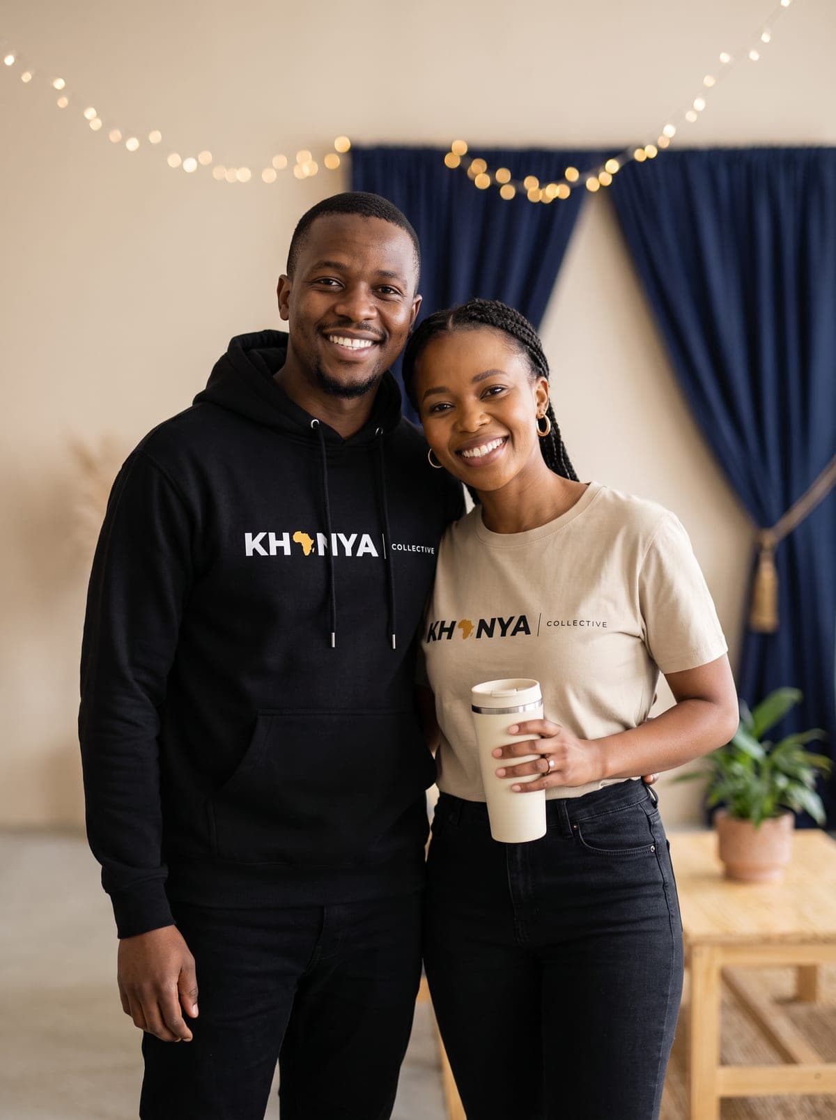 Two smiling creatives at an event wearing a black Khanya Collective hoodie and a sand Khanya Collective T-shirt