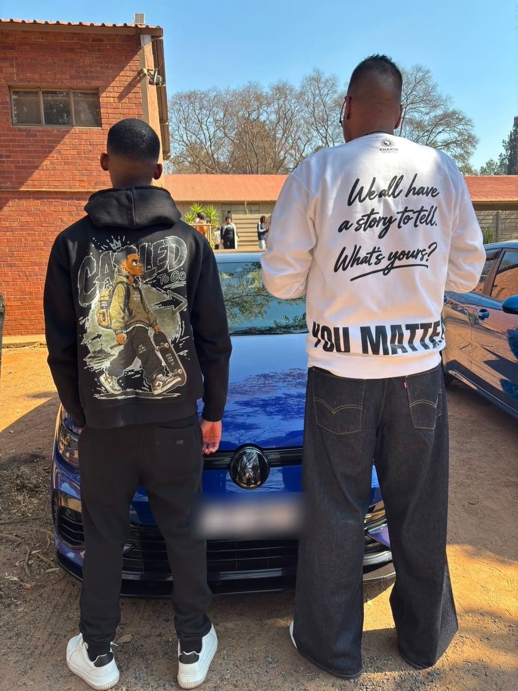 Two people wearing Khanya Collective apparel, a custom printed hoodie and a 'We all have a story to tell, You Matter' crewneck